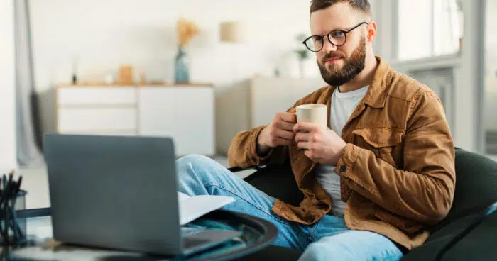 man watching movie online on laptop drinking coffee at home