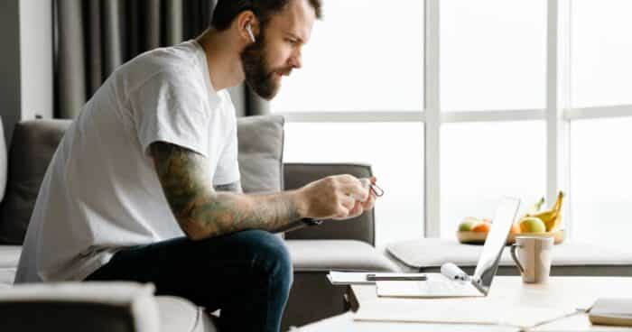 bearded european man using earphones while working with laptop at home